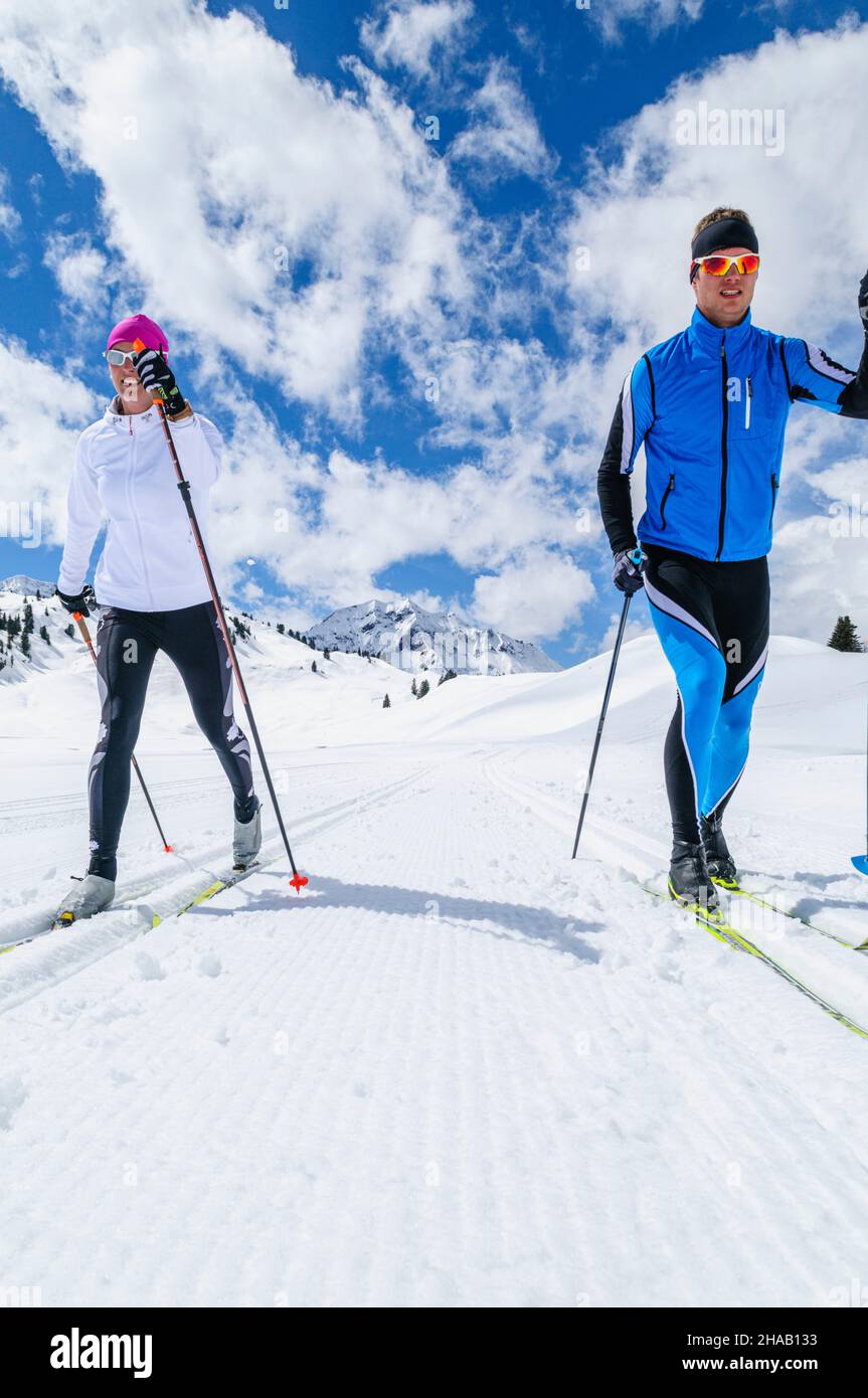 Two crosscountry skiers are running in the classic style on a high mountain trail near the