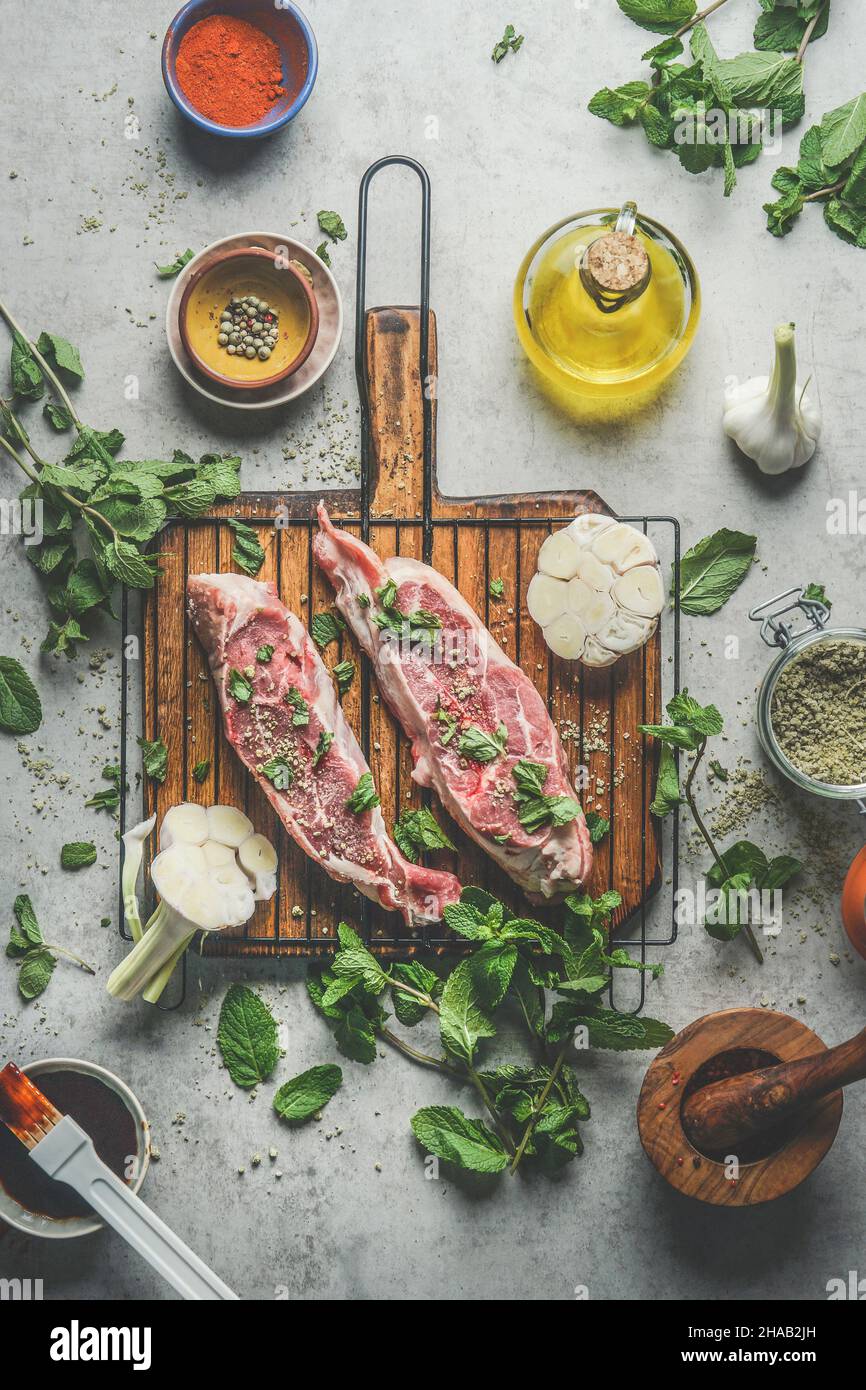 Raw meat with ingredients on wooden cutting board at  kitchen table background with fresh cooking ingredients: olive oil, garlic, herbs and spices. To Stock Photo