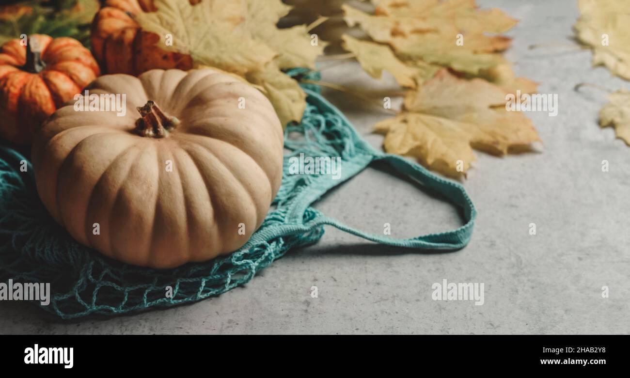 Pumpkin in blue reusable shopping bag at kitchen table with yellow autumn leaves. Sustainable plastic free grocery shopping with seasonal vegetables. Stock Photo