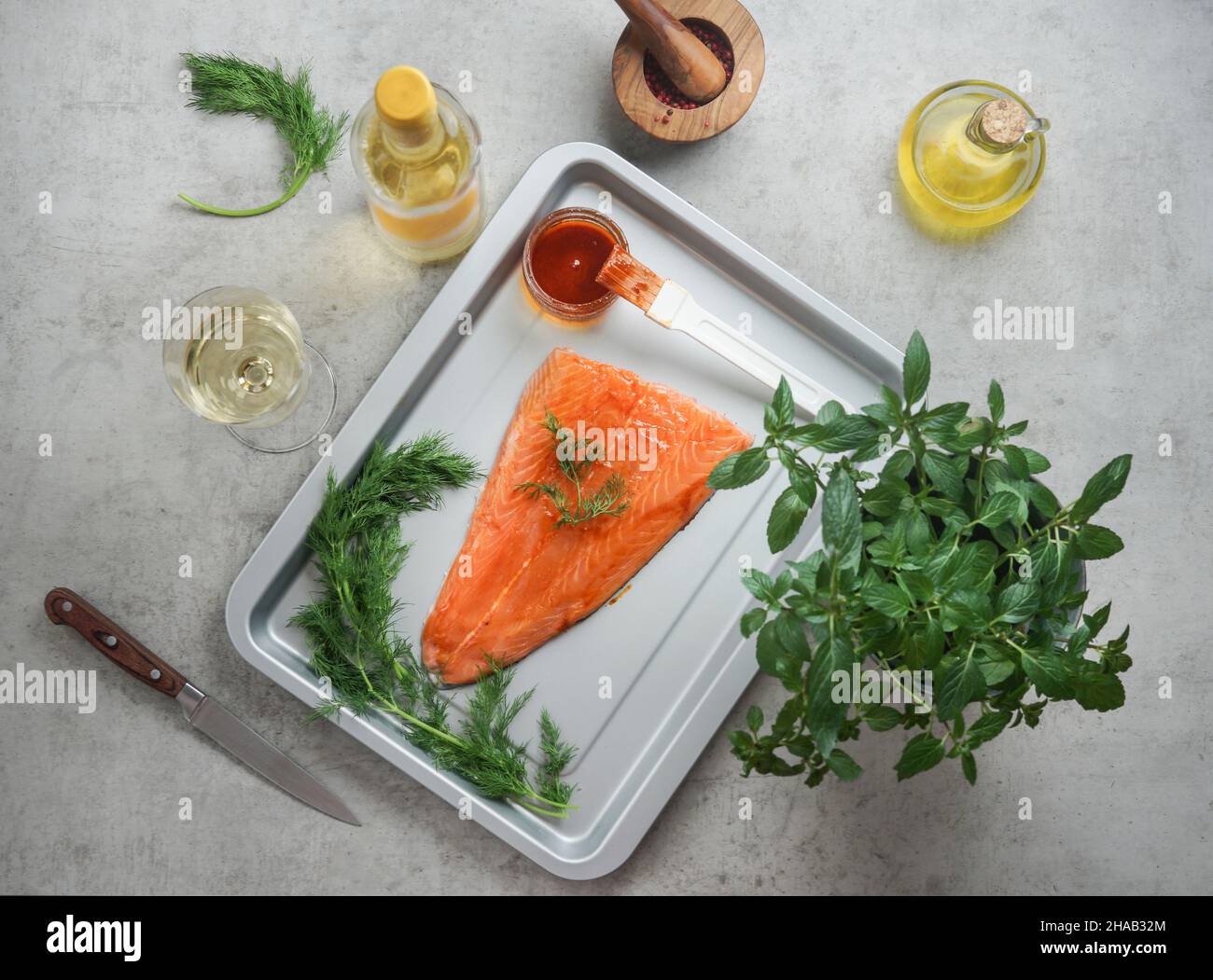 Preparation of salmon fish fillet on baking tray with healthy ingredients: herbs, spices, wine, oil and kitchen utensils on table. Healthy cooking wit Stock Photo