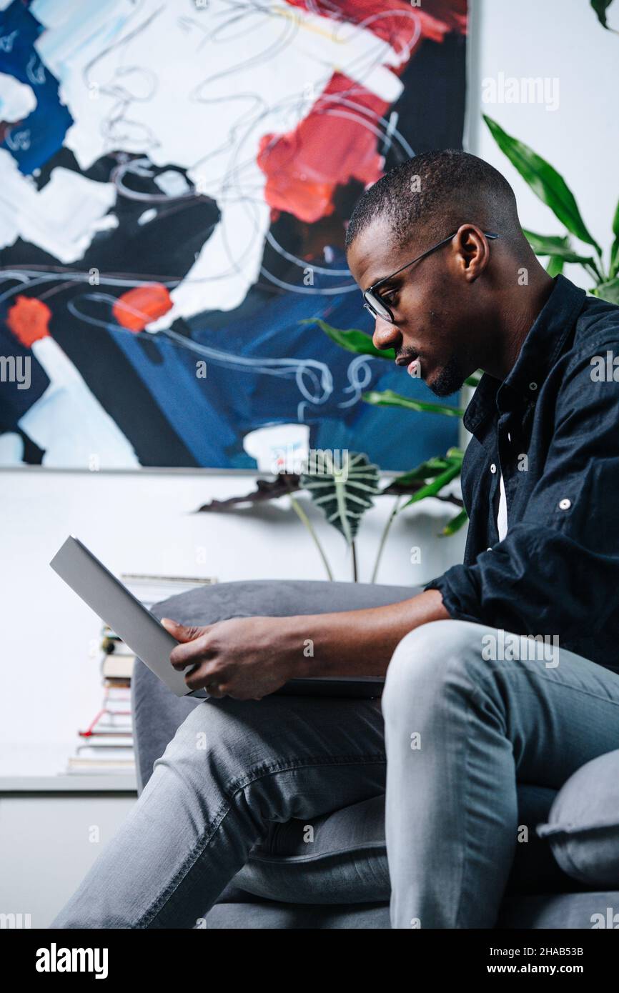 Side view african american man sitting on a sofa with a laptop in his ...