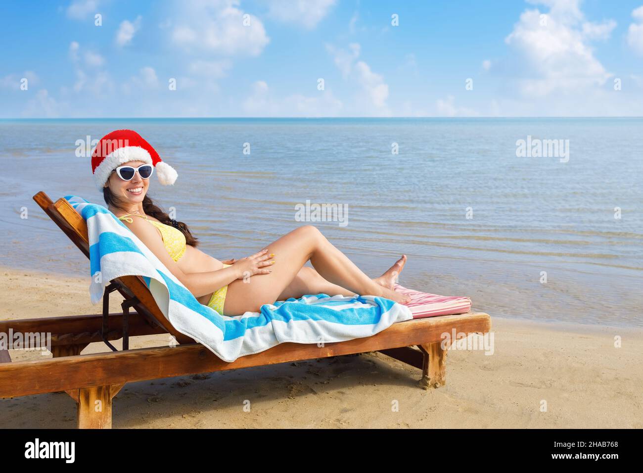 smiling young woman in santa hat and sunglasses lying on sun lounger Stock Photo