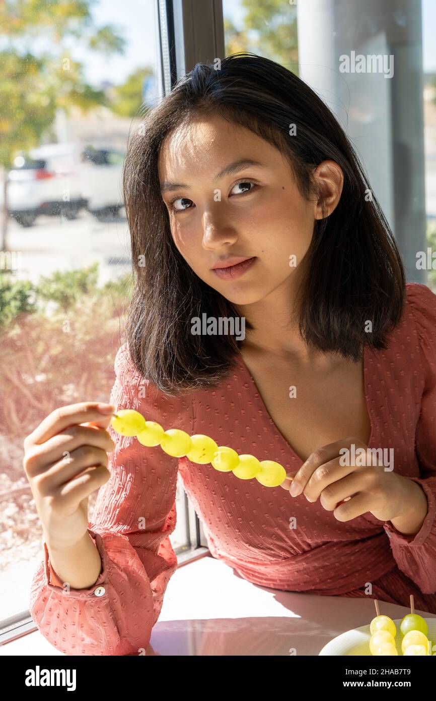 portrait of an Asian girl holding a skewer of grapes in her hands, vertical picture Stock Photo