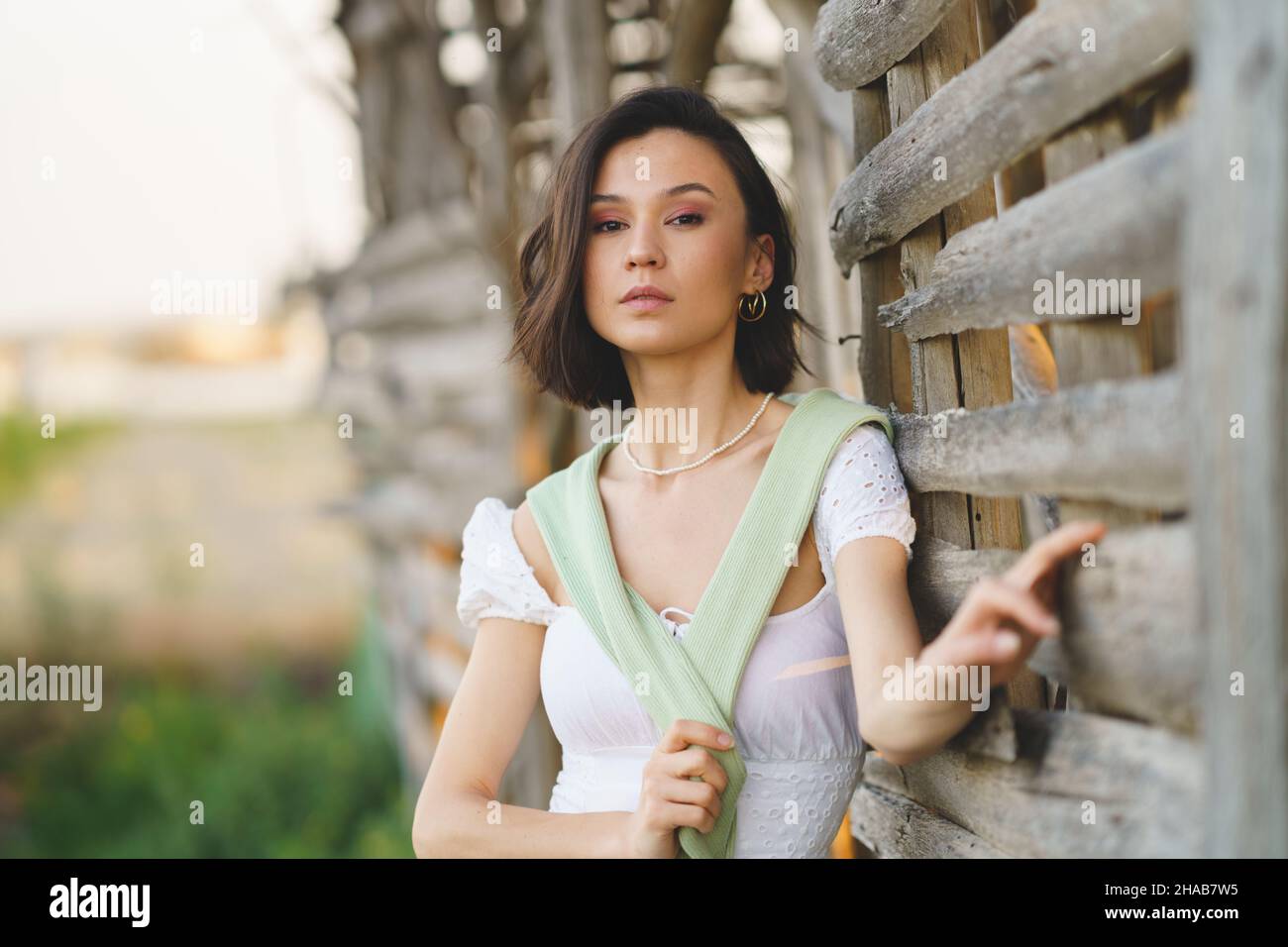 Asian woman, posing near a tobacco drying shed, wearing a white dress and green wellies. Stock Photo