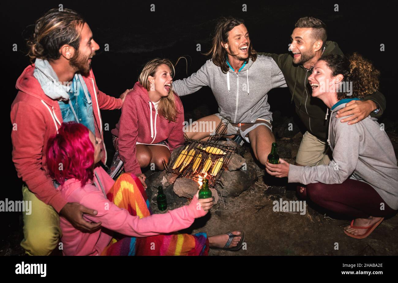 Young indie friends having fun together at night beach party cooking cobs at campfire - Friendship travel concept with alternative people travelers Stock Photo