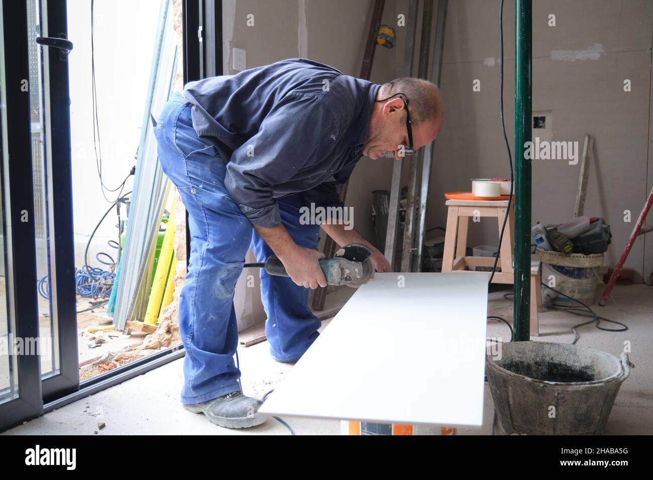 Senior constructor worker cutting a white ceramic tile with a radial saw. Stock Photo