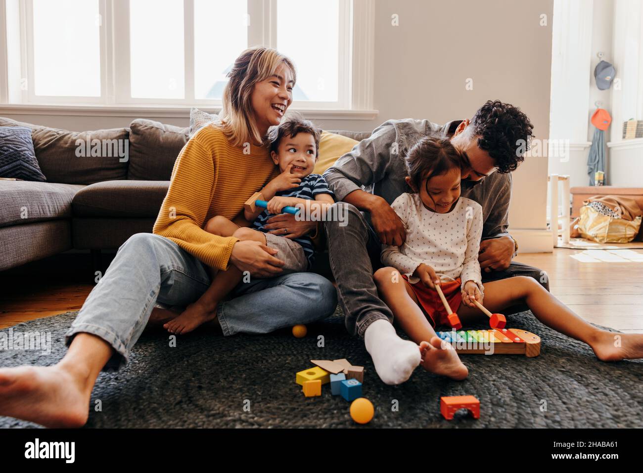 Young parents playing with their son and daughter in the living room. Mom and dad having fun with their children during playtime. Family of four spend Stock Photo