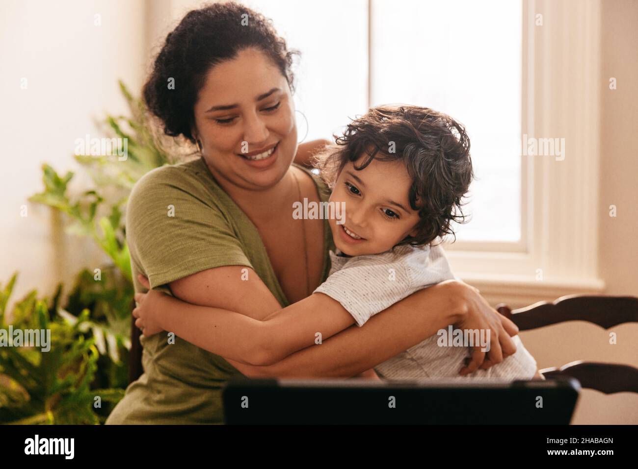 Supportive mother embracing her son while watching an online tutorial. Mother and son smiling happily while looking at a digital tablet. Loving single Stock Photo
