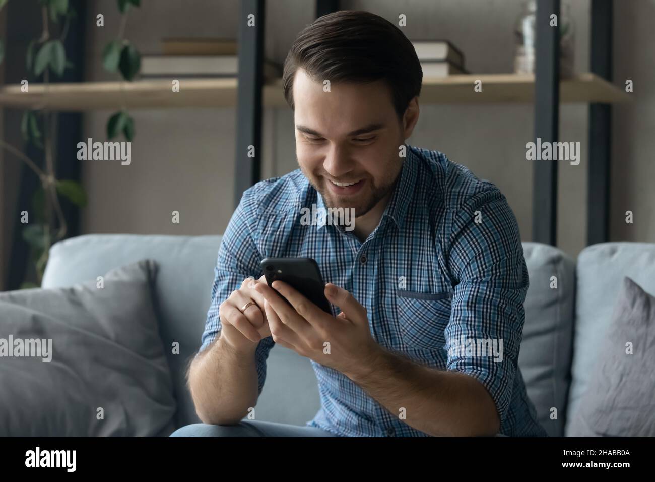 Smiling young man sit on couch with smartphone Stock Photo