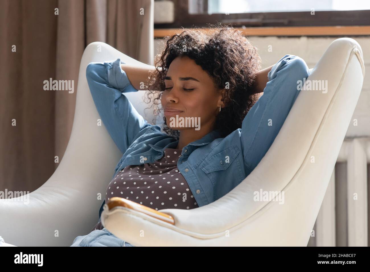 Serene African woman put hands behind head relaxing on armchair Stock Photo