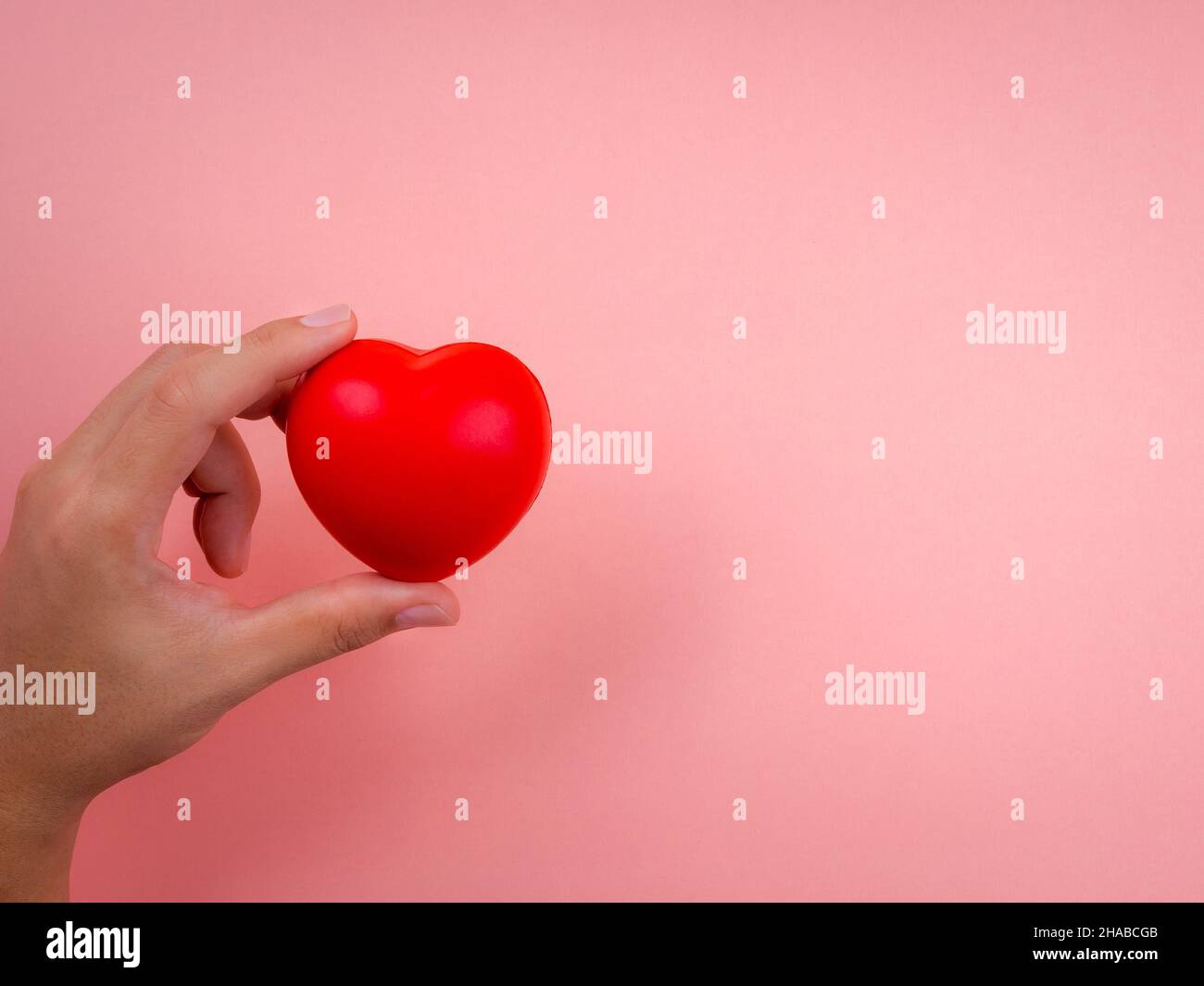 Hand holding the red heart ball on pink pastel background with copy ...