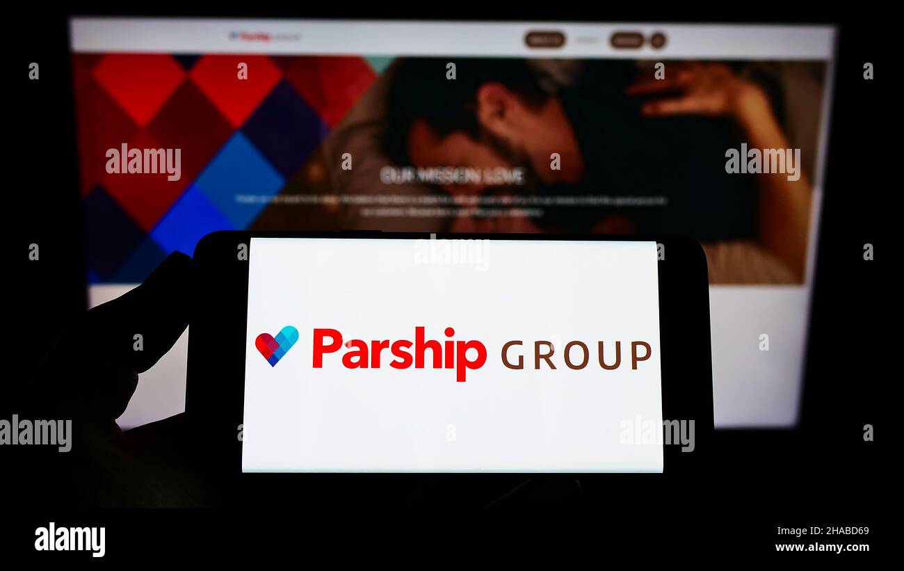 Person holding smartphone with logo of online dating company ParshipMeet Holding GmbH on screen in front of website. Focus on phone display. Stock Photo