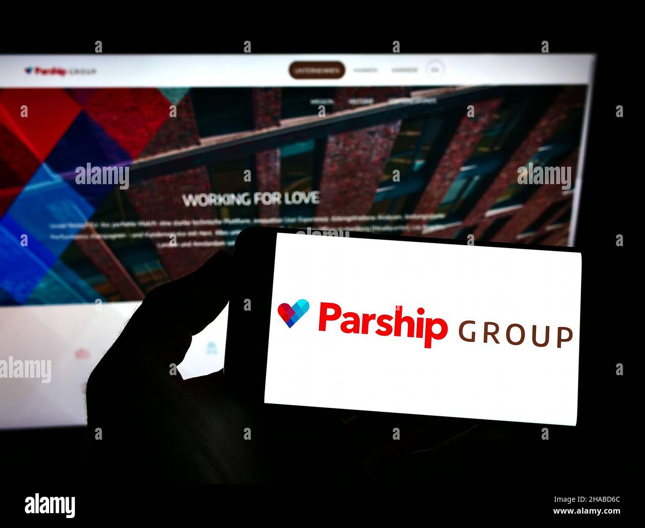 Person holding mobile phone with logo of online dating company ParshipMeet Holding GmbH on screen in front of web page. Focus on phone display. Stock Photo