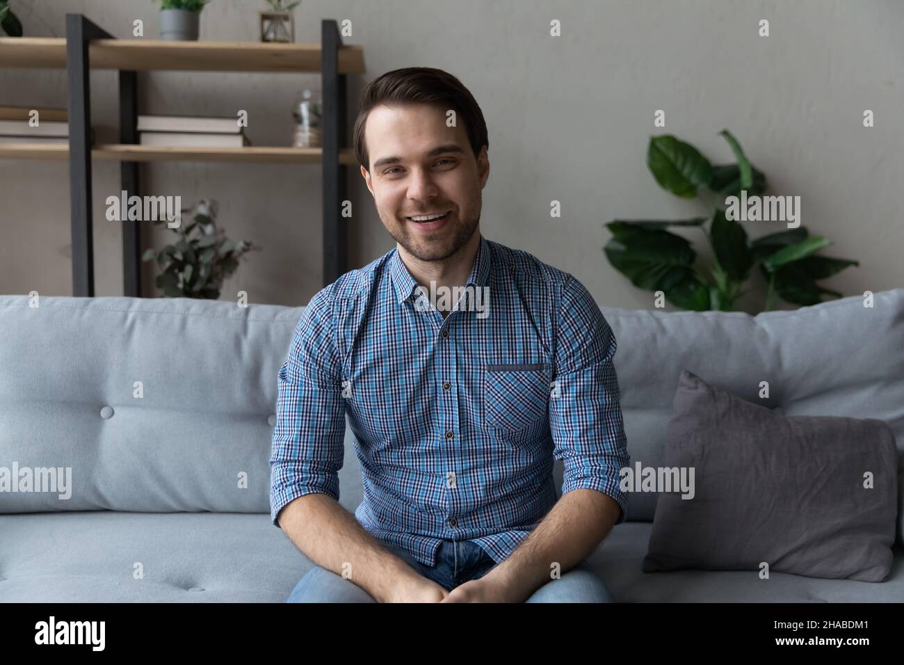 Smiling young man sit on sofa looking at camera Stock Photo