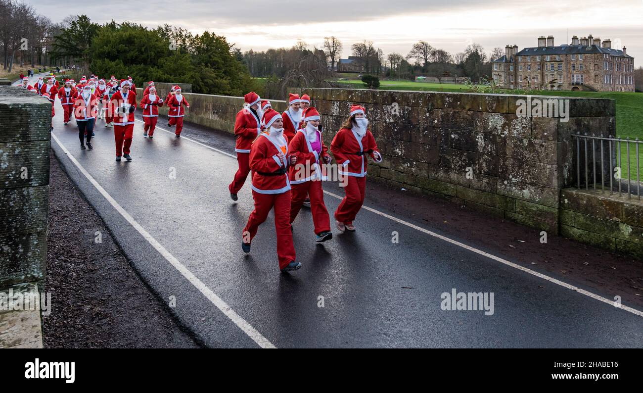 Dalkeith, Midlothian, Scotland, United Kingdom, 12th December 2021. Santa Run and Elf Dash: the charity fund-raising event takes place in Dalkeith Country Park to raise money for CHAS (Children’s Hospices Across Scotland) Pictured: participants in the Santa Run dressed in Santa costumes running across the old stone Montagu Bridge Stock Photo