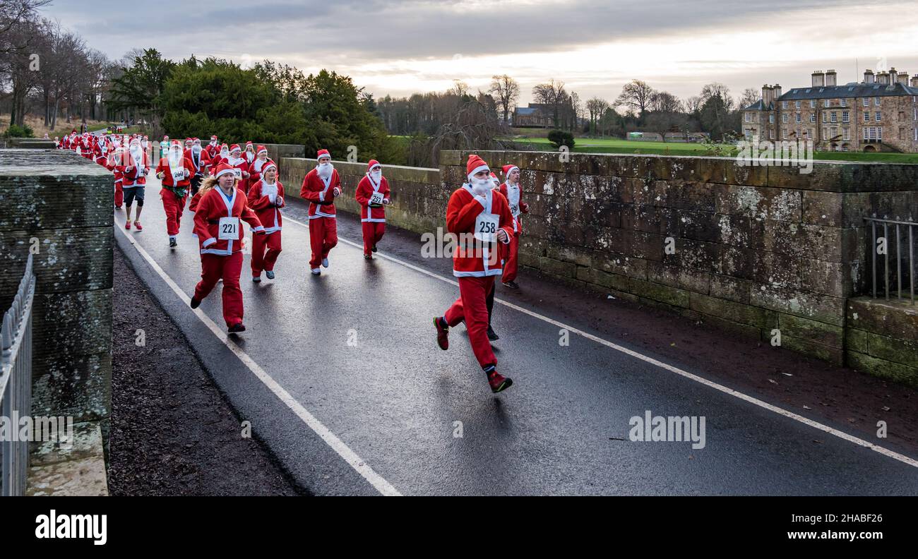 Dalkeith, Midlothian, Scotland, United Kingdom, 12th December 2021. Santa Run and Elf Dash: the charity fund-raising event takes place in Dalkeith Country Park to raise money for CHAS (Children’s Hospices Across Scotland) Pictured: participants in the Santa Run dressed in Santa costumes running across the old stone Montagu Bridge Stock Photo
