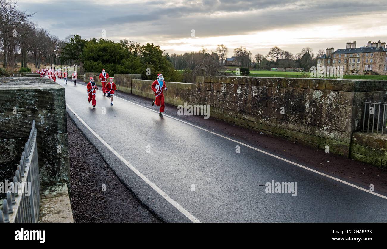 Dalkeith, Midlothian, Scotland, United Kingdom, 12th December 2021. Santa Run and Elf Dash: the charity fund-raising event takes place in Dalkeith Country Park to raise money for CHAS (Children’s Hospices Across Scotland) Pictured: participants in the Santa Run dressed in Santa costumes running across the old stone Montagu Bridge Stock Photo