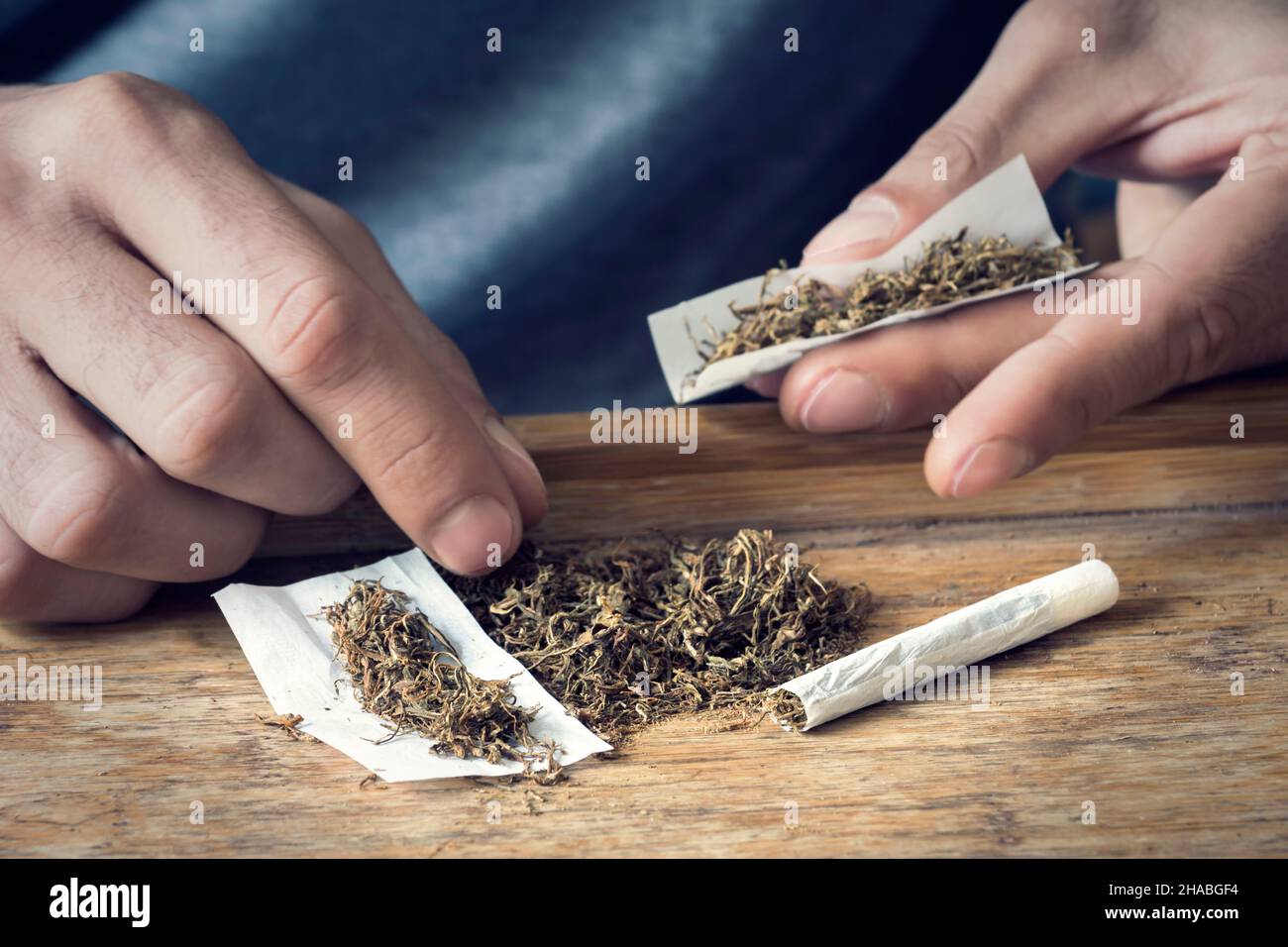 Loose rolling tobacco with hands of a man rolling a cigarette in the background Stock Photo