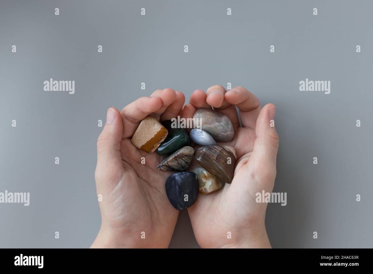 child holding various semiprecious stones in hands on gray background Stock Photo