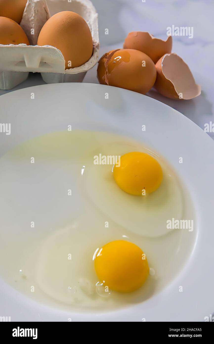 Raw Eggs off the shell on a white plate. Egg carton with eggs on the side. Stock Image. Stock Photo