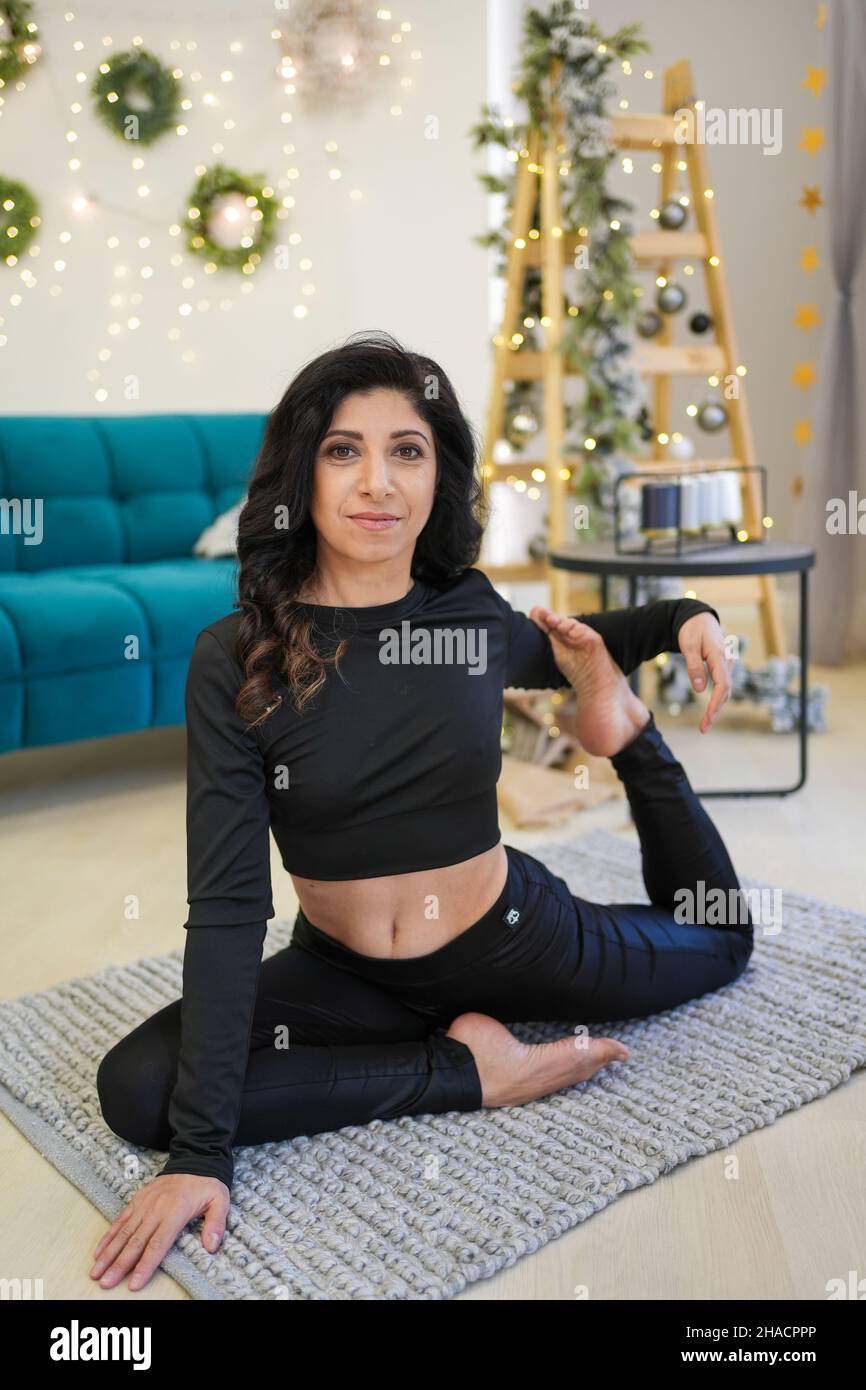 Middle age woman doing yoga near sofa and Christmas tree in home Stock Photo