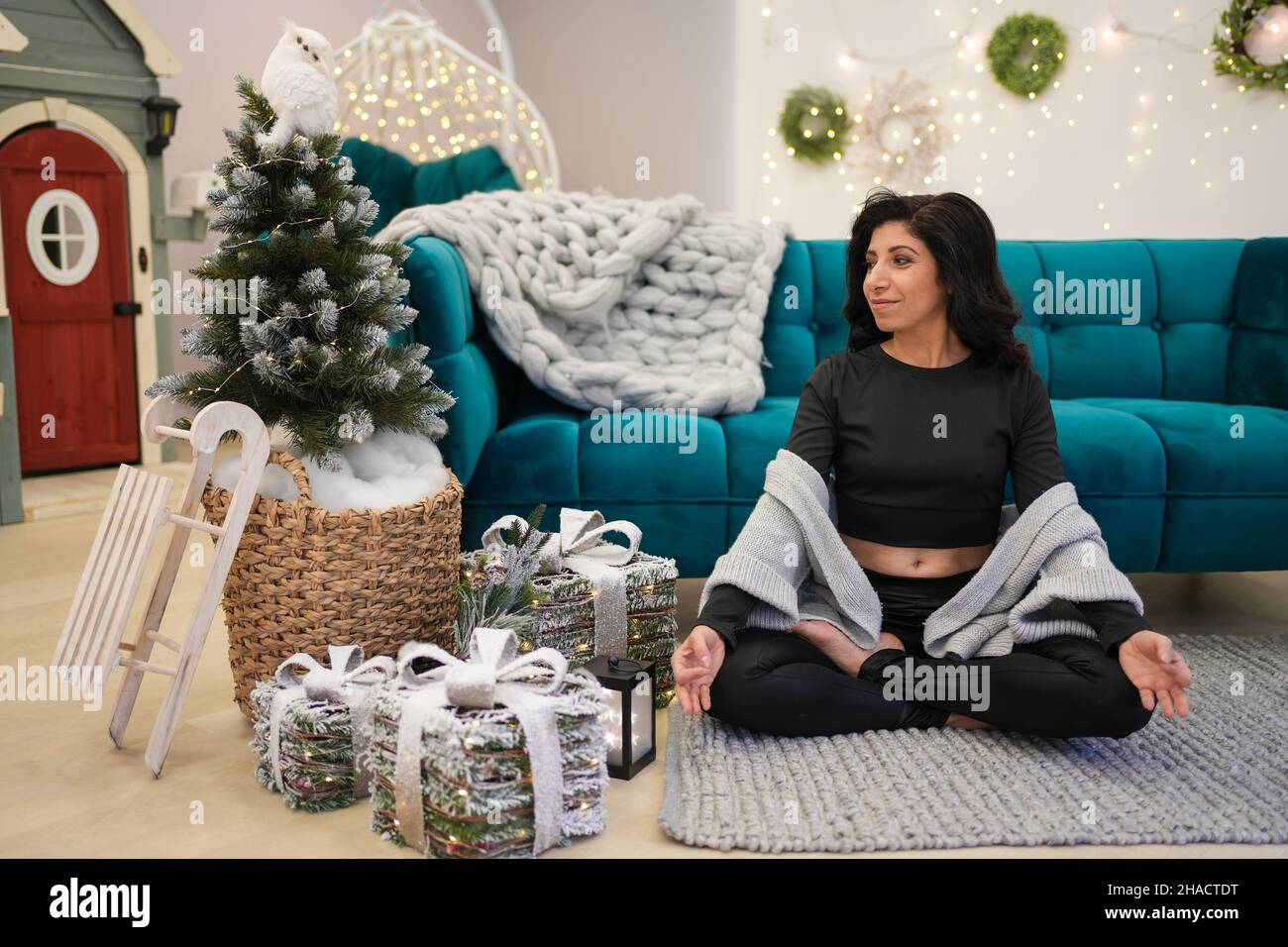Portrait of middle age woman meditating while sitting near sofa and Christmas tree Stock Photo