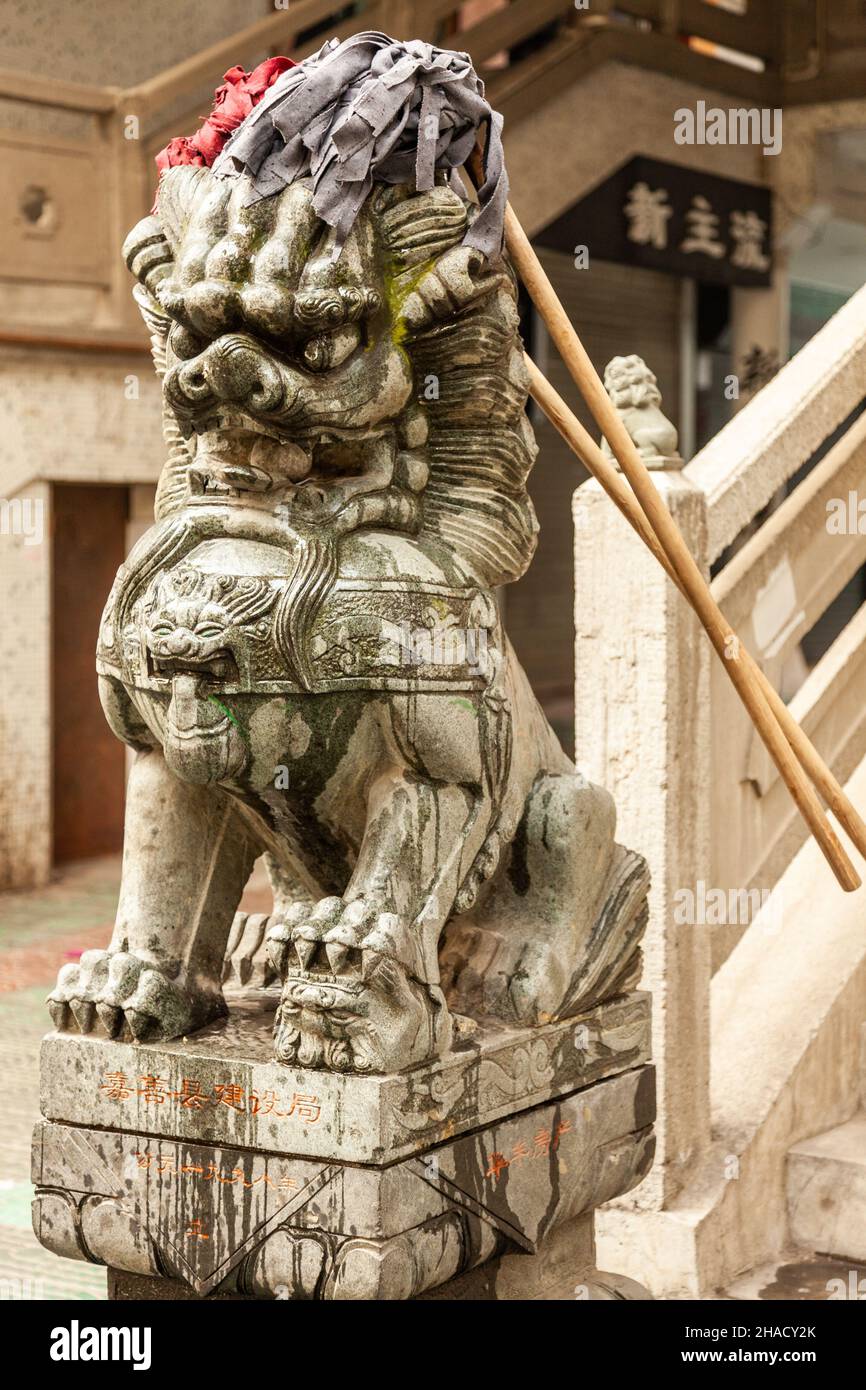Stone lion at the entrance of a building, wearing mops. Jiashan, China Stock Photo