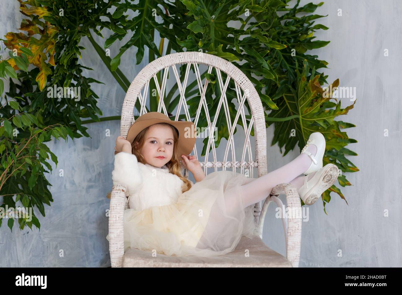 beautiful little girl in a hat and a dress sitting in a chair Stock ...