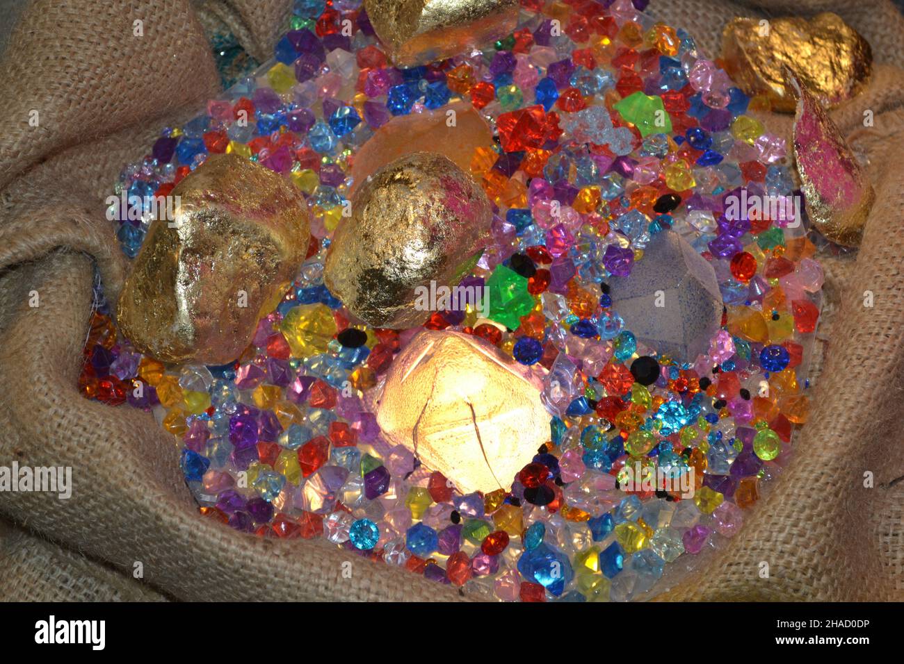 Mixed Acrylic Plastic Crystal Gems as Treasure Hunting Pirate Jewelry in Burlap Sack for Fashion Store Window Merchandising. Glow in the Dark. Stock Photo