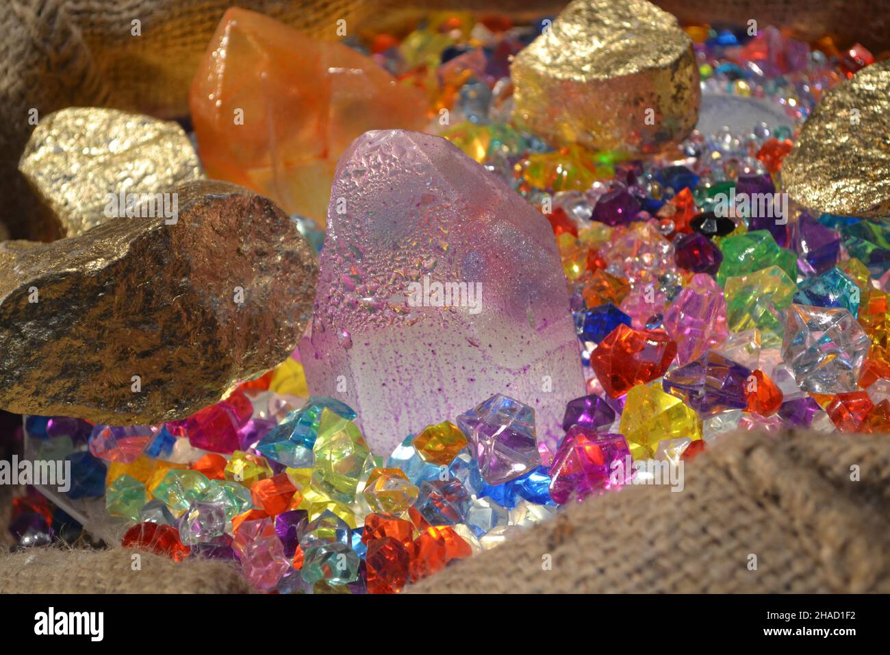 Mixed Acrylic Plastic Crystal Gems as Treasure Hunting Pirate Jewelry in Burlap Sack for Fashion Store Window Merchandising. Stock Photo