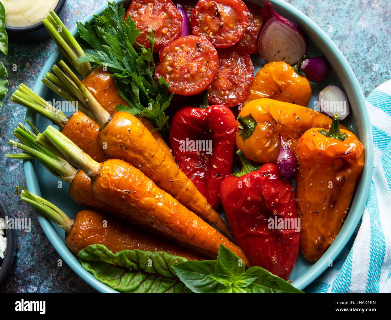 baked grill baby carrots, tomato, bell pepper in a plate, basil and spices vegan dish, close up, white sauce Stock Photo
