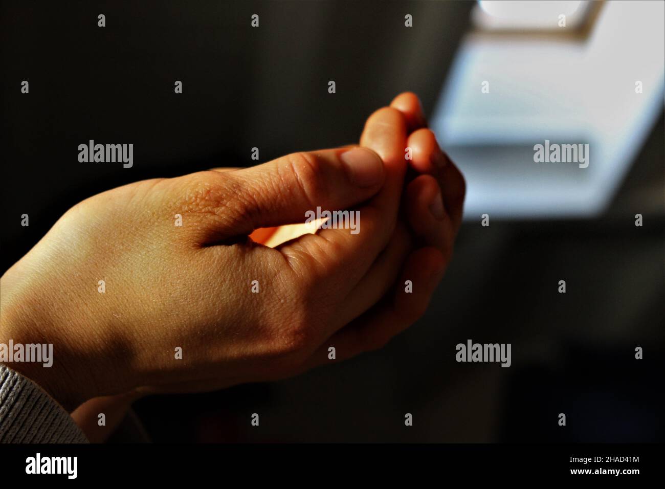 Woman cupping hands in the light on a dark background ready to receive something in her palms. Religious concept, receiving eucharist Stock Photo