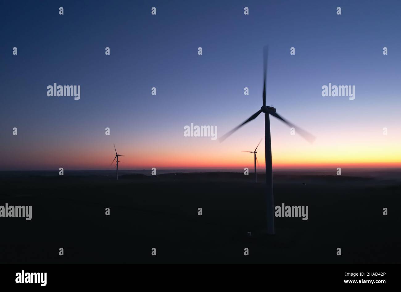 Three silhouettes of rotating propellers of wind turbines against the background of the night sky. Stock Photo