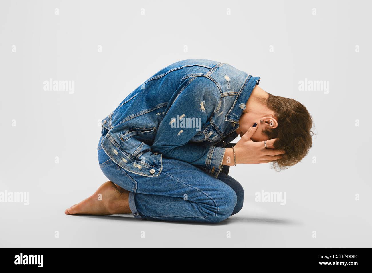 Desperate young man kneels on the floor and covers face with hands ...