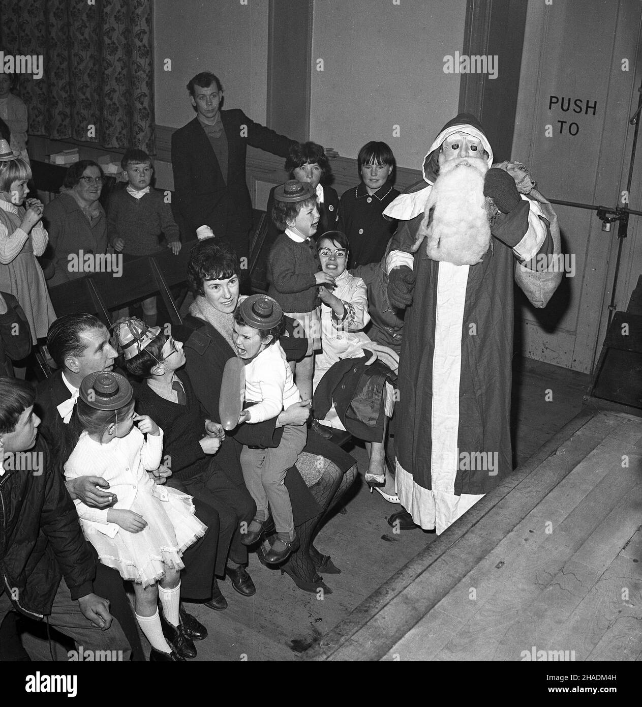 1965, historical, in a village hall, a scary santa claus, little girls held by their parents frightened by the a santa claus with a face mask and false beard, Fife, Scotland, UK Stock Photo