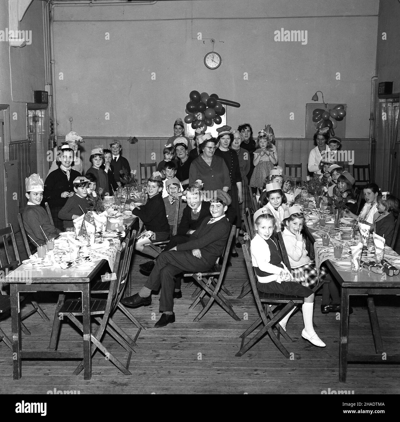 1965, historical, group of children and some adults at a village Christmas party, Longwick village hall, Buckinghamshire, England, UK. Food and drinks laid out on traditional wooden tressel tables. Stock Photo