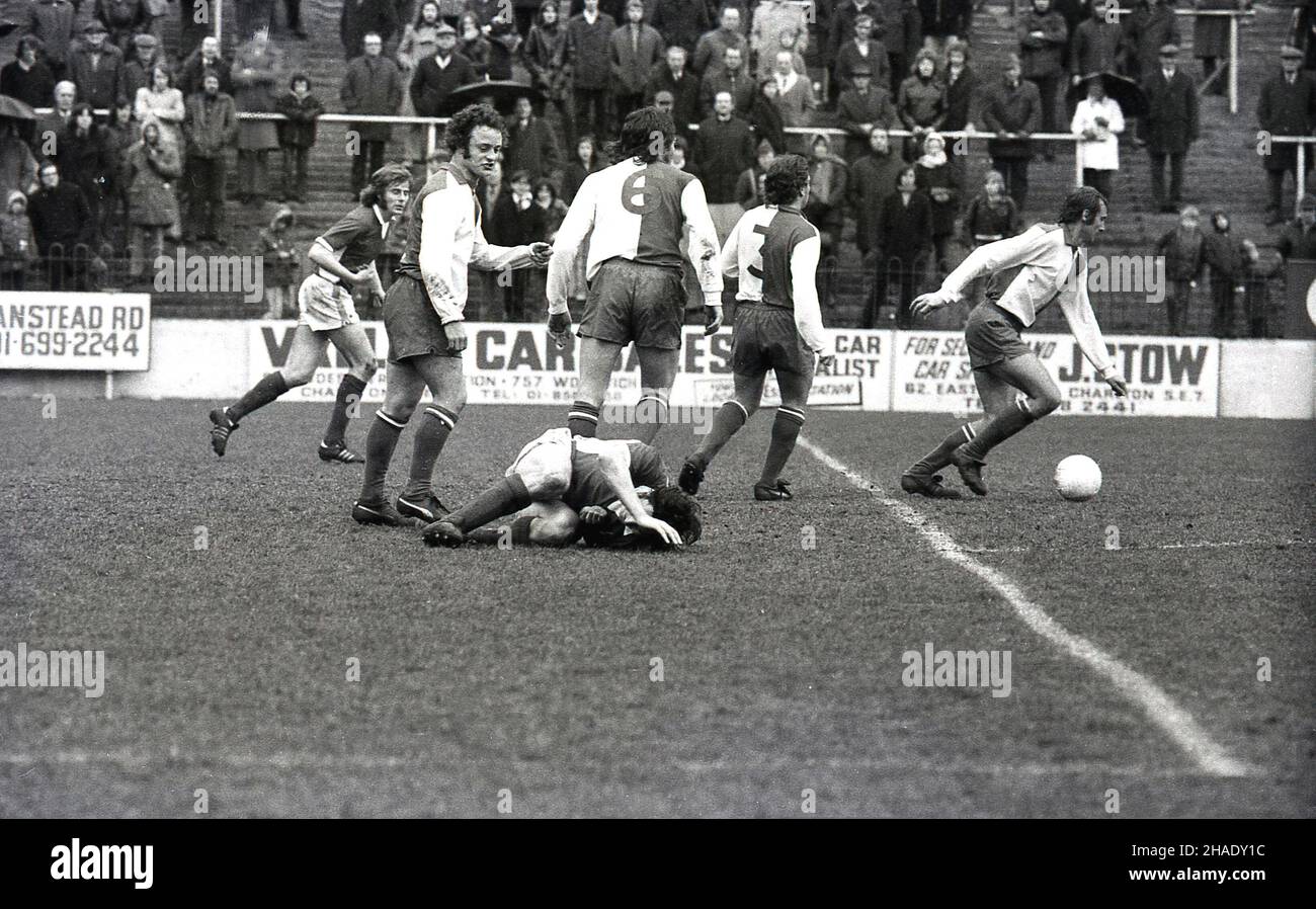 1973, historical, a football match at The Valley, South-east London, England, UK, home of Charlton Athletic FC. in a match against Blackburn,  a player is on the ground injured after a tackle but play continues. Fans  or supporters stand on the banked terraces, some behind a steel barrier, watching the game. Charlton Athletic FC was founded in 1905 and they have played at the Valley since 1919. Stock Photo