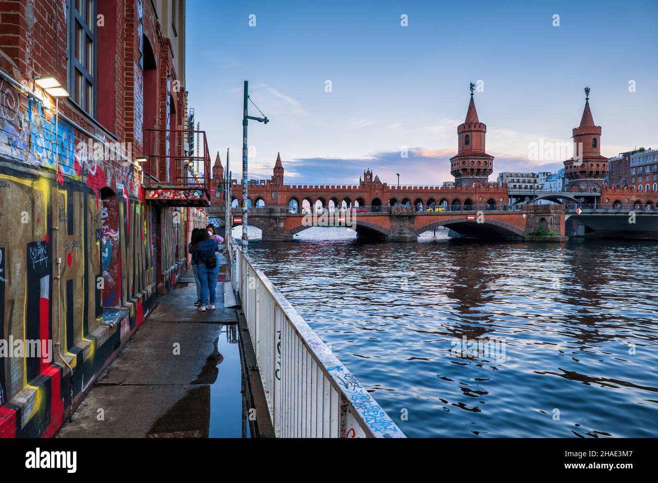 City of Berlin, Germany, view from riverside below The Wall Museum building to Oberbaum Bridge (Oberbaumbrücke) over river Spree, early evening. Stock Photo
