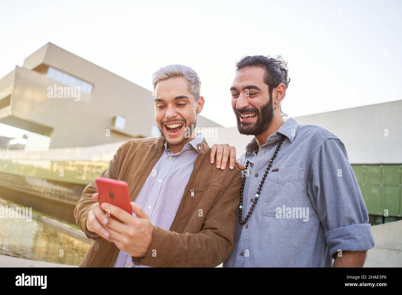 Smiling gay couple together using phones. Happy people watching something at mobile cell. Stock Photo