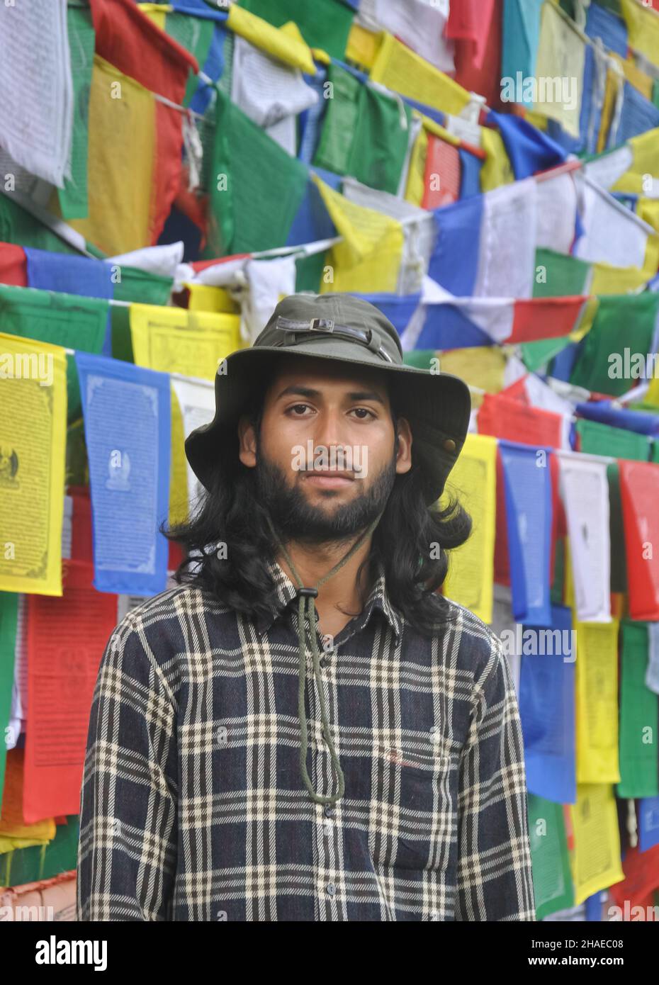 A bearded and long haired male tourist looking at camera while standing against Buddhist prayer flags Stock Photo