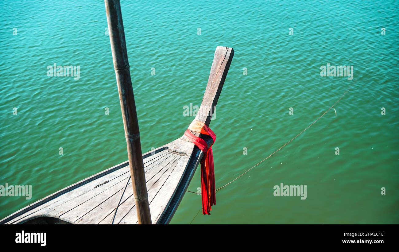 Photos of the bow ship head with red cloth tied. View from head of traditional wooden boat with red cloth tied. fishing boat, traditional thailand lon Stock Photo