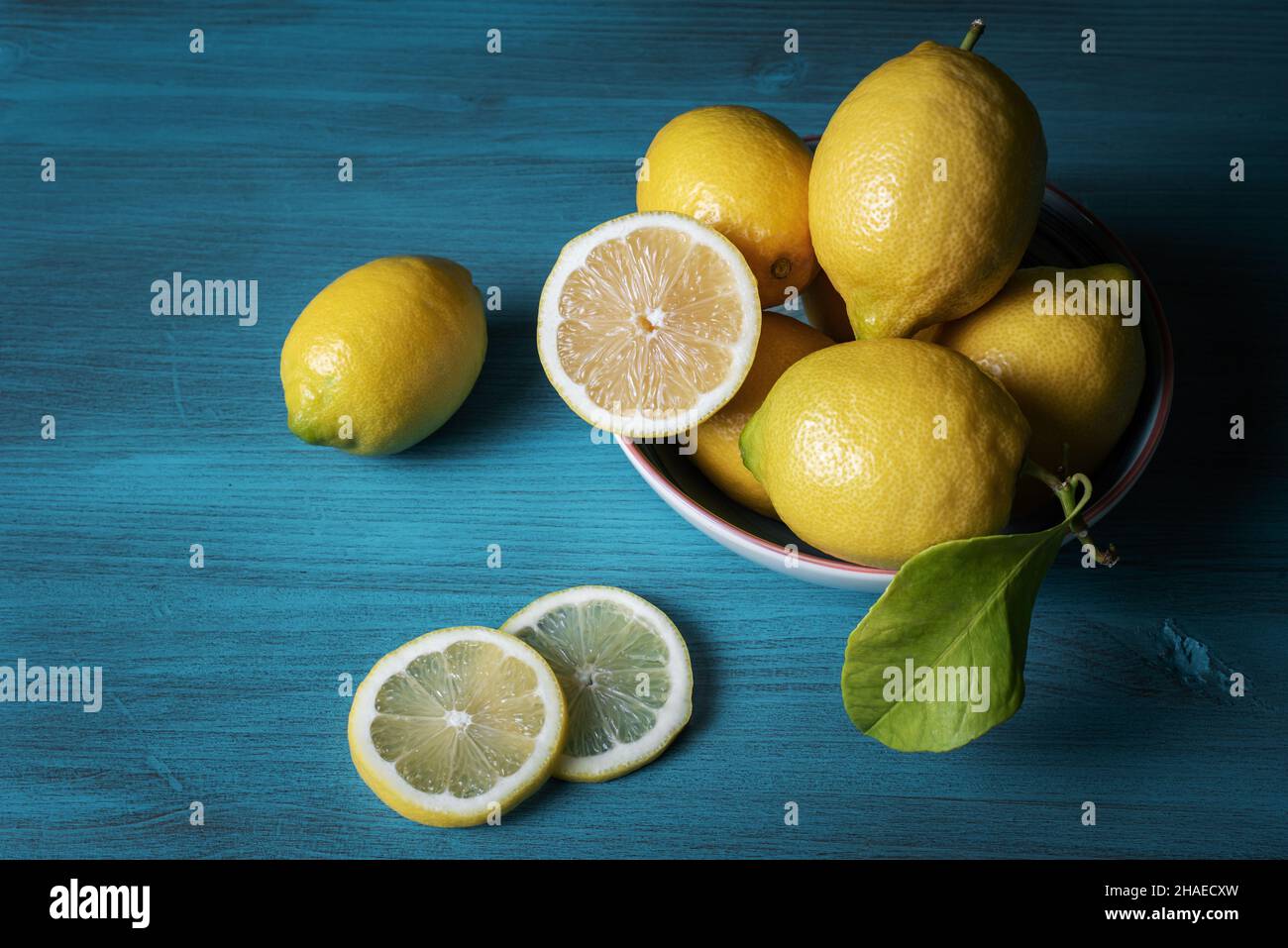 Lemons in a bowl and two loose slices, all on a light blue wooden table. Stock Photo