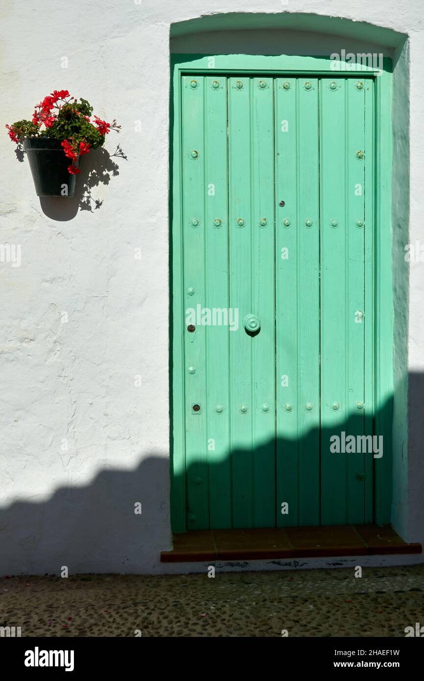 Green wooden door in a Mediterranean Andalusian house with a white facade with a pot of red flowers Stock Photo