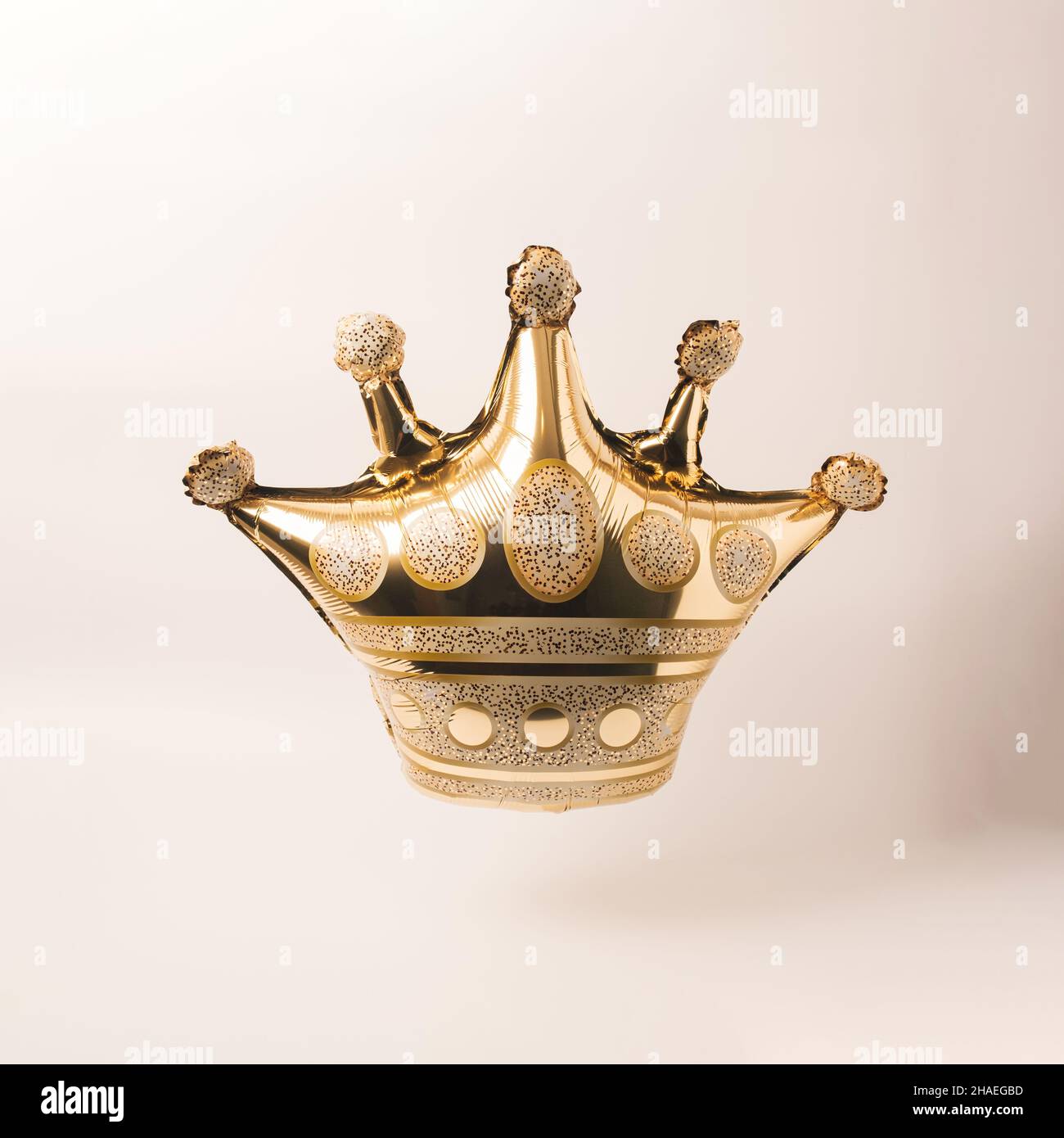 Golden crown shaped floating balloon on a beige background. Minimal New Year celebration concept. Stock Photo