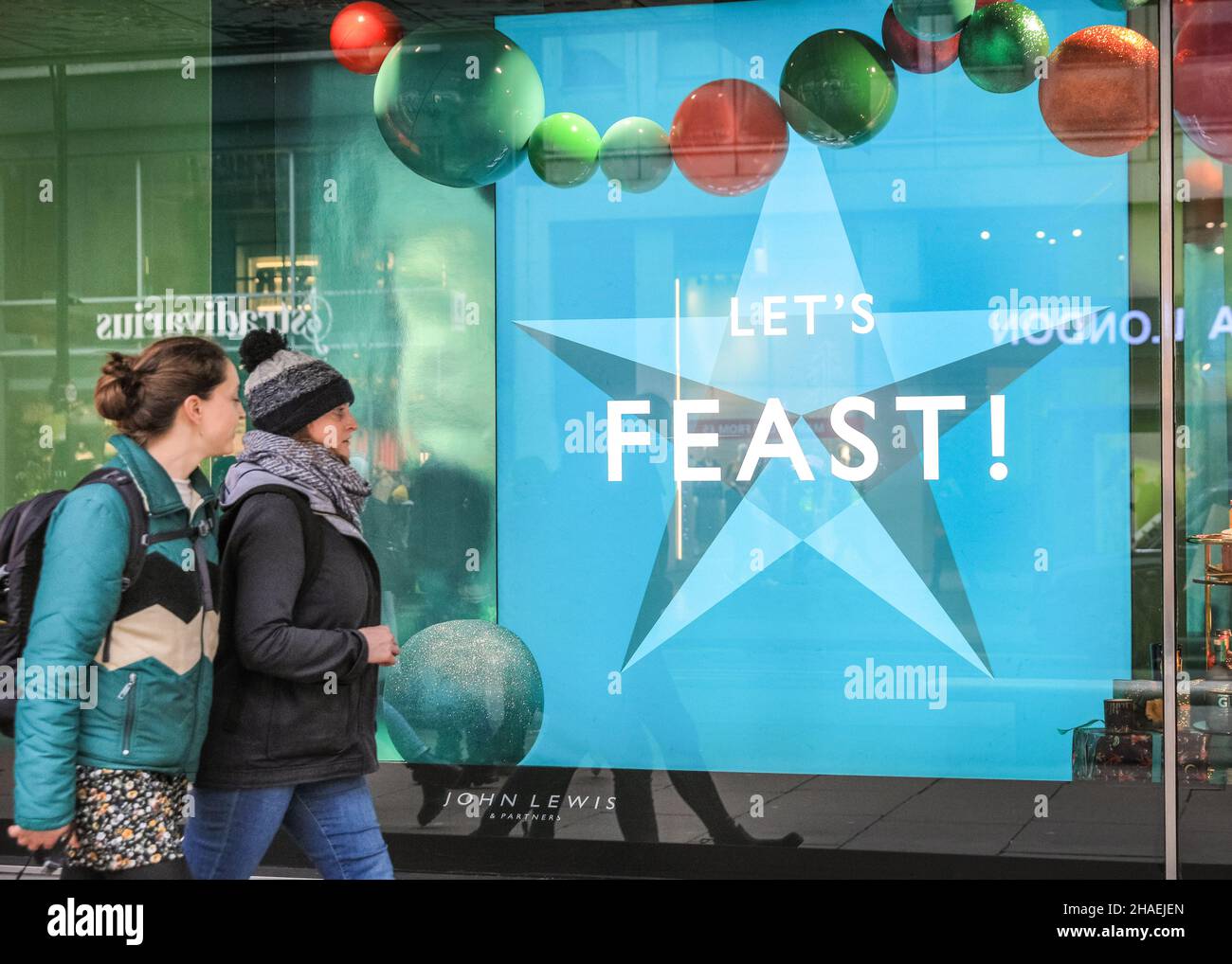 Oxford Street London, UK, 12th Dec 2021. People look at colourful window decorations and messages at John Lewis. Shoppers and visitors to London crowd into busy Oxford Street today despite infection rates with the new omnicron covid variant in London, and the wider country, rising fast, and government considering the introduction of further measures to curb the trend. Stock Photo