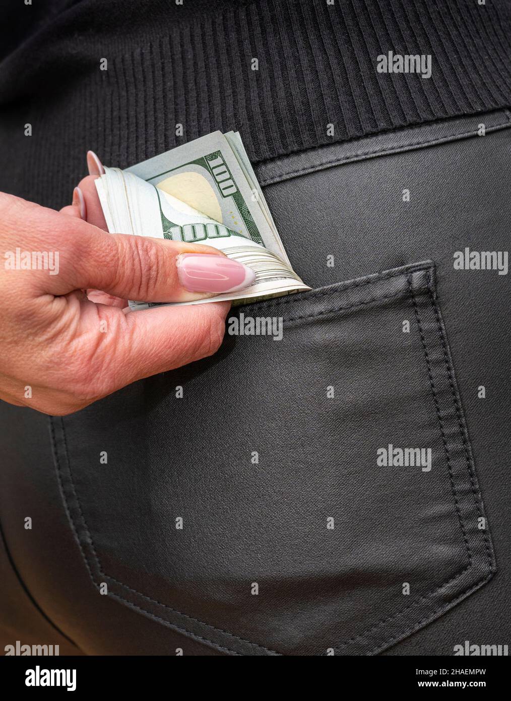 Attractive female placing wad of cash into back pocket of her jeans. Out of pocket expenses
