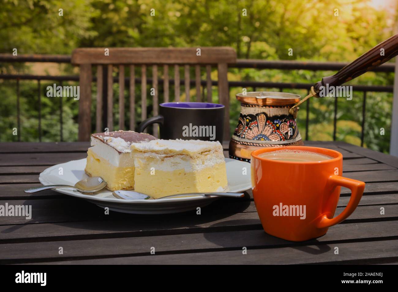 Rustic breakfast. Wooden coffee table with coffee cups, cezve, lake Bled cream cake, delicious slovenian dessert. Kremna Rezina or Cremeschnitte Stock Photo