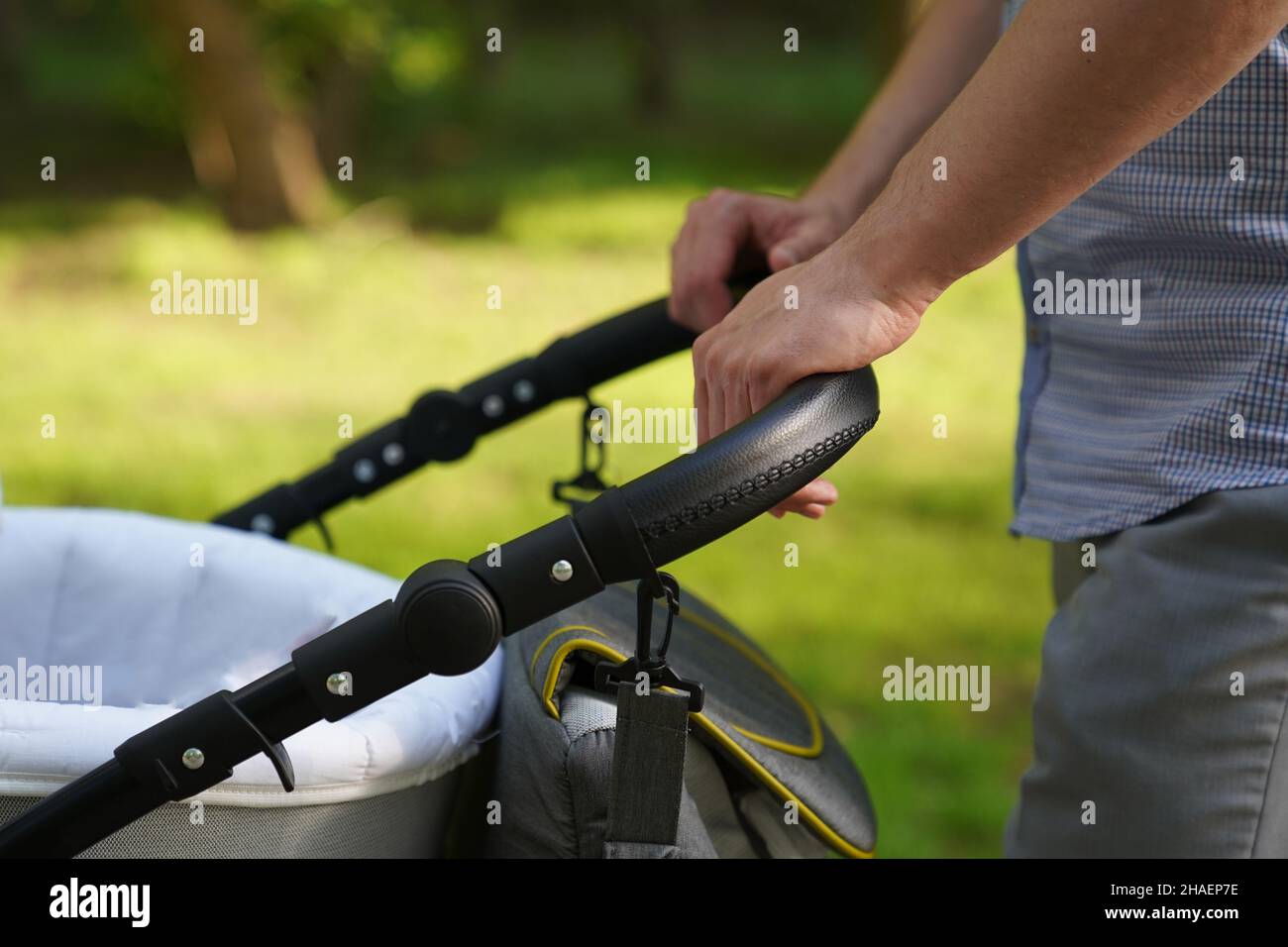 Close-up of men's hands with a stroller, a young dad walking in the park with a baby in a stroller, fatherhood, dad, father's day concept. High quality photo Stock Photo