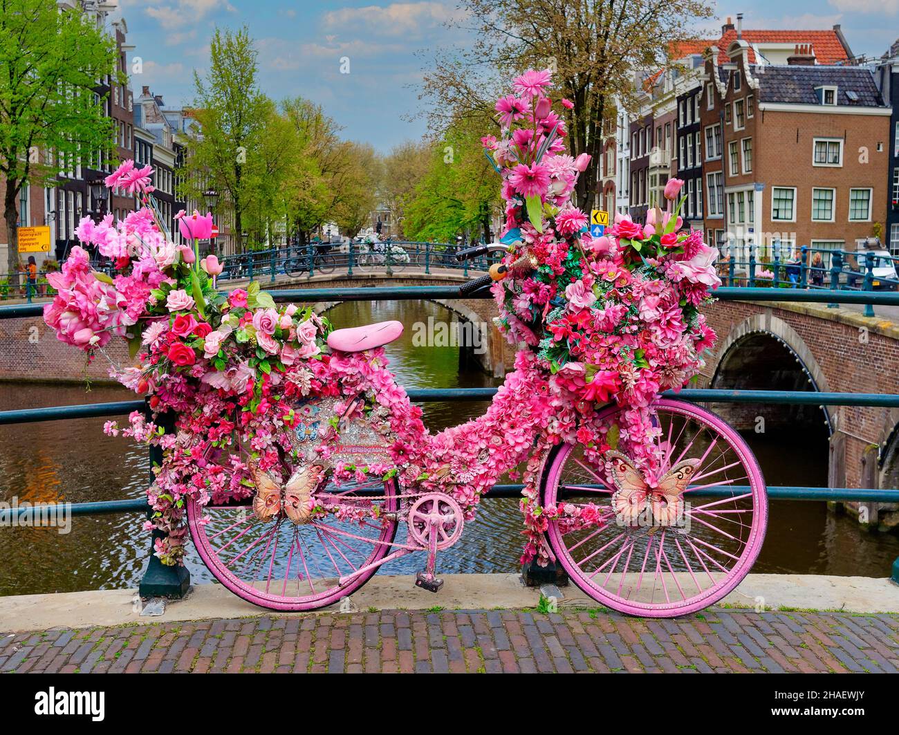 Old vintage bicycle decorated with pink flowers on small bridge in old part of Amsterdam Stock Photo