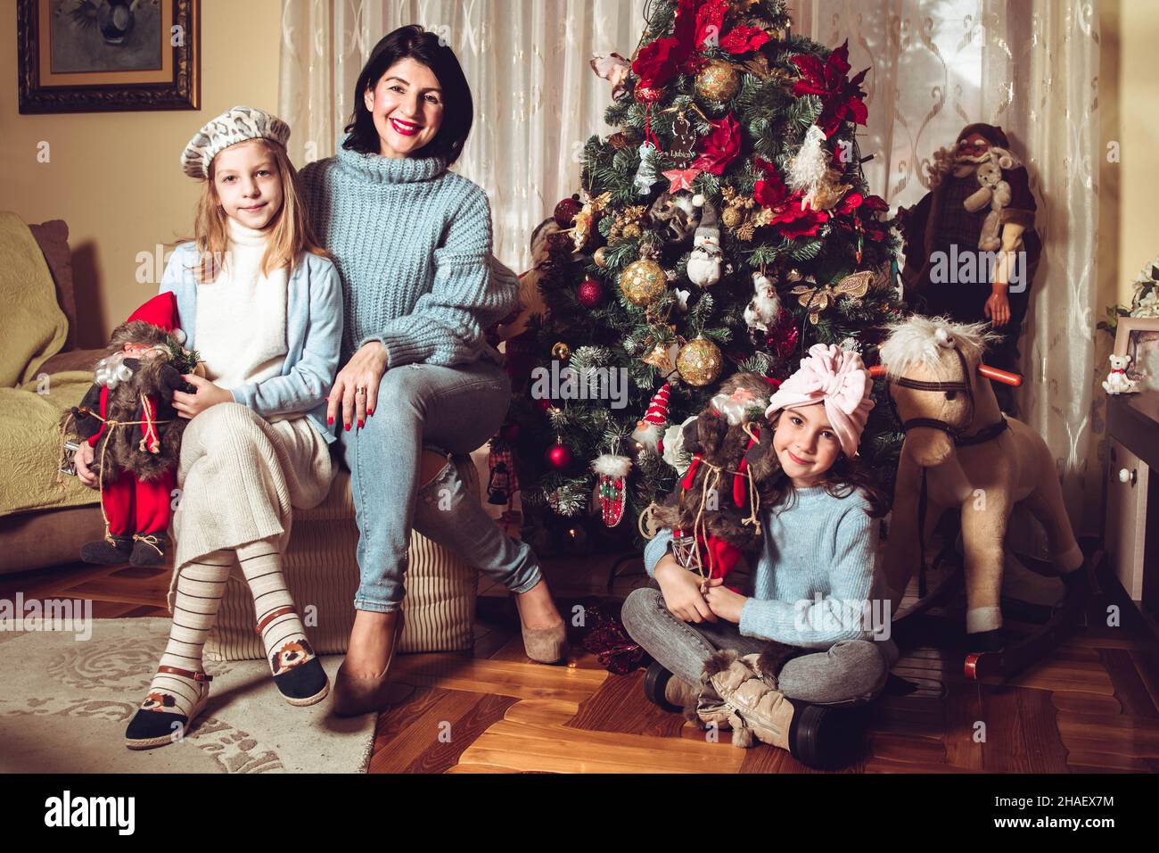 Mother and daughters sitting by the Christmas tree. Family holiday time Stock Photo